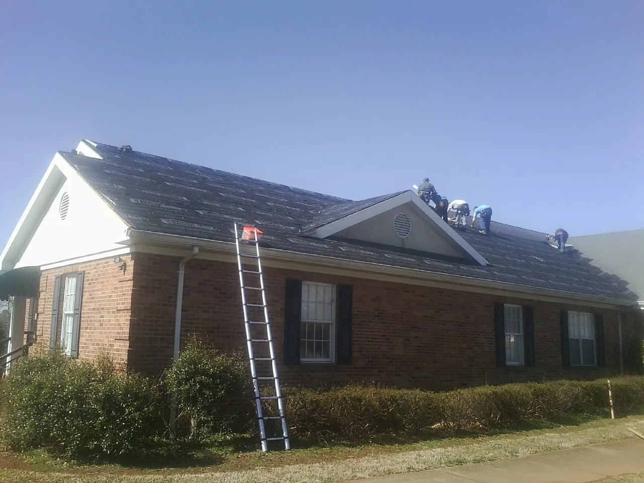 Crew tearing shingles off a brick ranch roof with a ladder set — Emergency Roof Repair work by our crew in Pedro Bay