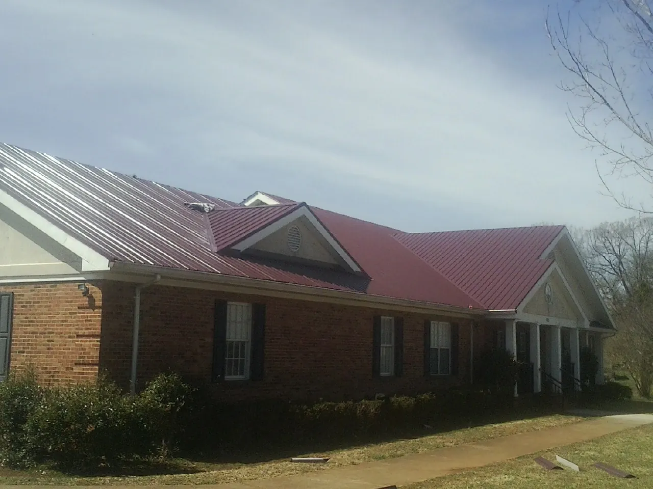 Red metal roof with gabled entries on a long brick building, from a Hail Damage Roof Repair job in Pedro Bay
