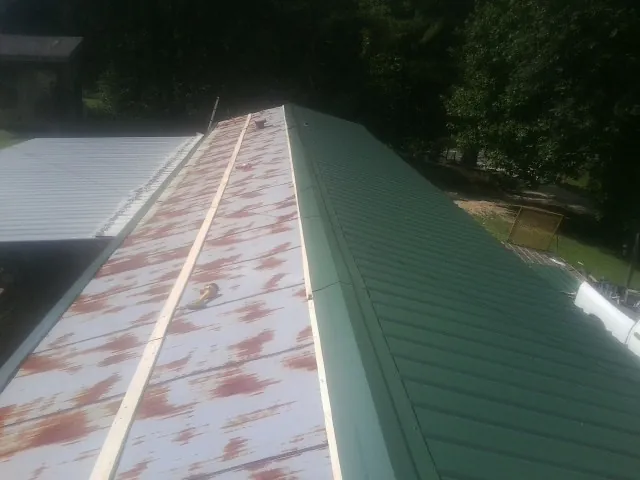 Old rusted panels beside newly installed green metal roofing — Wind Damage Roof Repair by Roofing Brothers in Pedro Bay