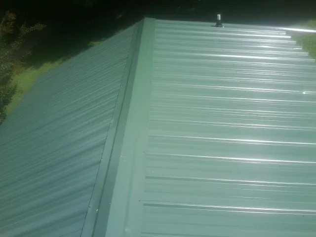New green metal panels meeting at the ridge of a roof — Flat Roof Repair work by our crew in Pedro Bay