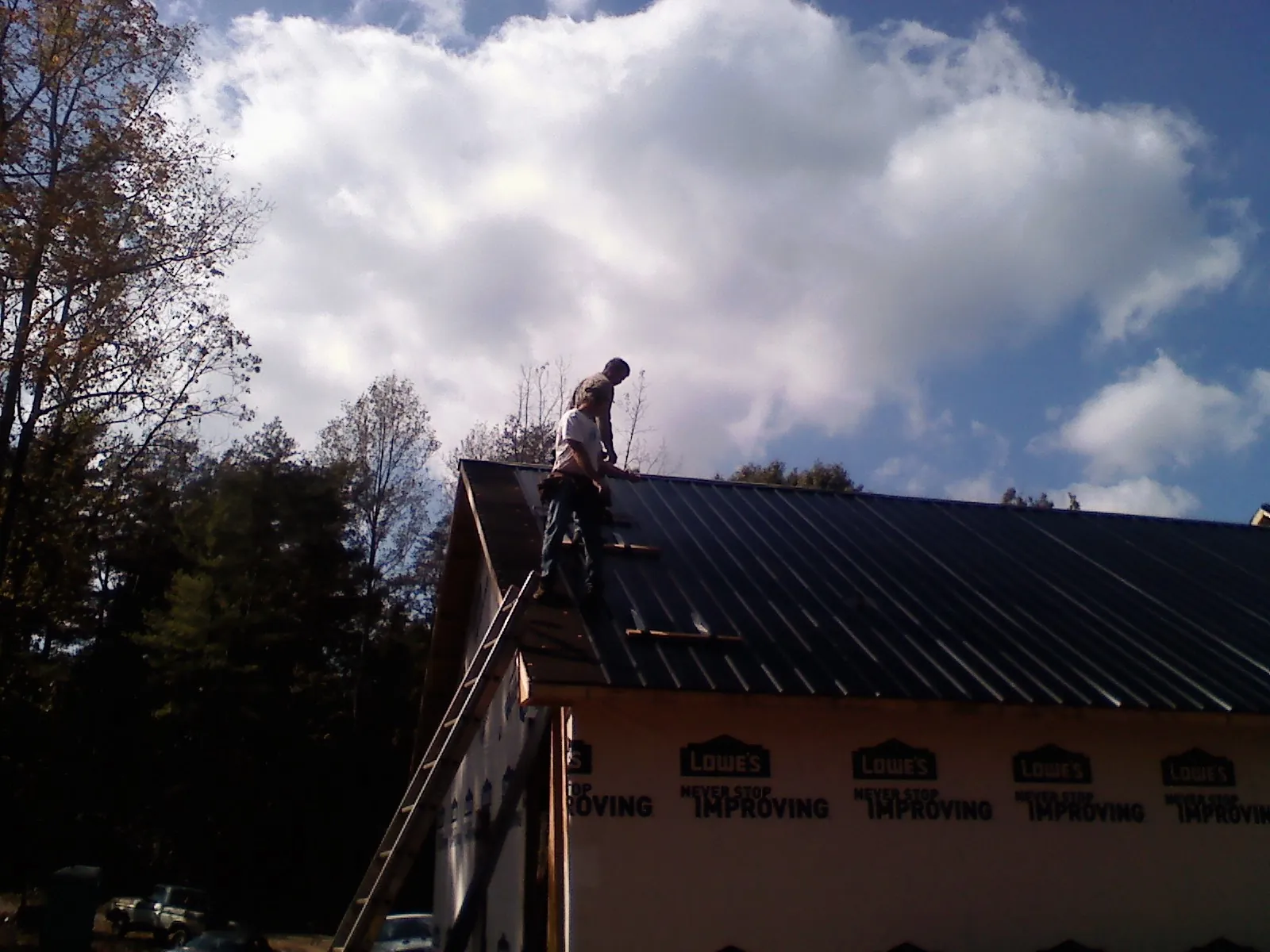 Roofer fastening dark metal panels high against a cloudy sky, from a Roof Inspection job in Pedro Bay