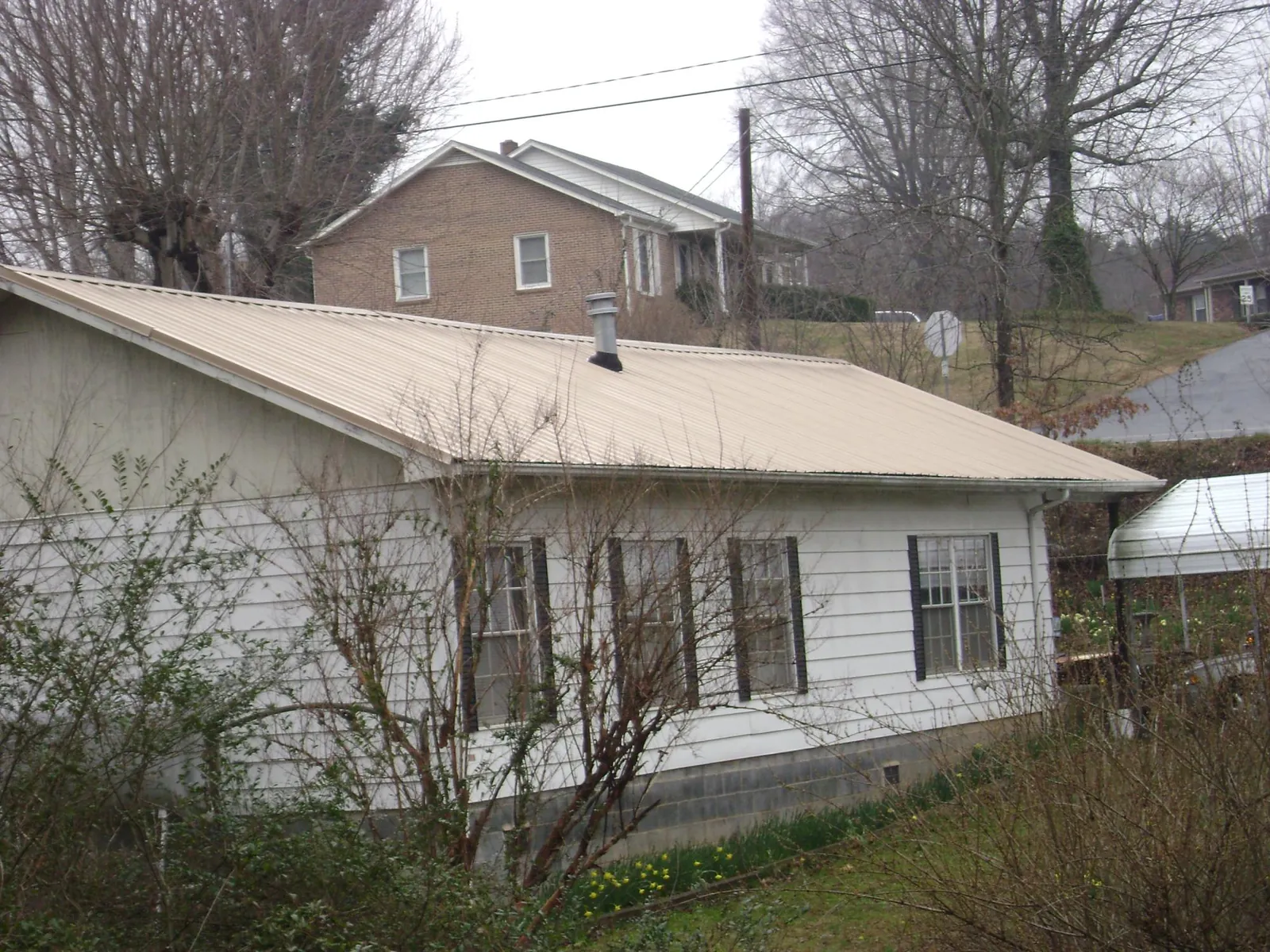 Tan metal roof on a white sided house set into a hillside — Commercial Roofing by Roofing Brothers in Pedro Bay